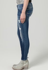 Jeans ajustados de color azul con detalles desgastados, con una cintura de altura media y un ajuste slim. Combinados con botas de tobillo grises.