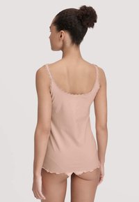 Woman with curly hair in a bun wearing a light pink lace-trimmed camisole and matching shorts, viewed from behind against a neutral background.