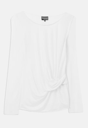 Camisa blanca de manga larga hecha de una tela suave, con un escote redondeado y un detalle anudado en el lateral con tela drapeada.