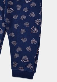 Námorní joggery s malými ružovými srdiečkami a logom 'GUESS', vyrobené z mäkkej látky s hladkou textúrou.