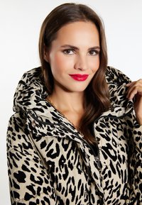 Jachetă pufă bej cu un imprimeu leopard negru îndrăzneț, glugă mare, închidere cu fermoar și un finisaj neted. Accentuata cu un detaliu din metal lucios.