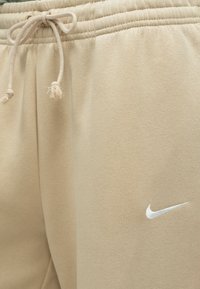 Μπεζ βαμβακερές φόρμες με ελαστική μέση, κορδόνι και κεντημένο λευκό λογότυπο Nike στο κάτω μέρος του ποδιού. Μαλακή υφή με άνετη, καθημερινή εφαρμογή.
