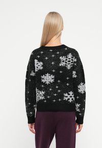 Schwarzer Strickpullover mit weißen Schneeflockenmuster und Sternen, mit einem gerippten Halsausschnitt und Bündchen. Weicher, strukturierten Stoff mit lockerer Passform.