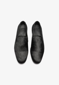 Schwarze Slipper mit einem glatten Lederfutter und einer strukturierten Felloberfläche. Verfügt über ein schlankes Design und eine abgerundete Zehenpartie. Keine sichtbare Hardware.