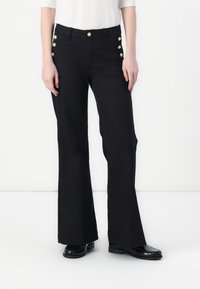 Pantalons évasés noirs avec une taille cintrée, ornés de boutons dorés sur le côté, réalisés dans un tissu lisse avec une finition élégante.