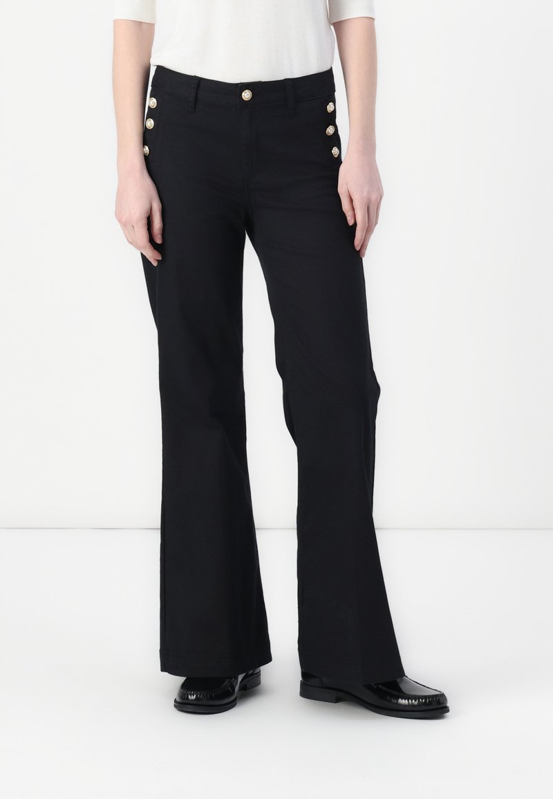 Pantalons évasés noirs avec une taille cintrée, ornés de boutons dorés sur le côté, réalisés dans un tissu lisse avec une finition élégante.