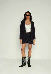 Musta bleiser valge korsetti ülaosa, must mini seelik ja mustad cowboy saapad valgete tikanditega. Mudel kannab musti prille.