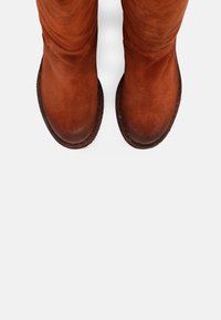 Paire de bottes en daim marron usées, vues de dessus sur un fond blanc uni, montrant des bouts arrondis et des semelles cousues.