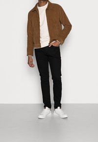 Hnědá kordová bunda, bílý svetřík s kulatým výstřihem, černé úzké džíny a bílé tenisky. Bunda má límec a přední zip.