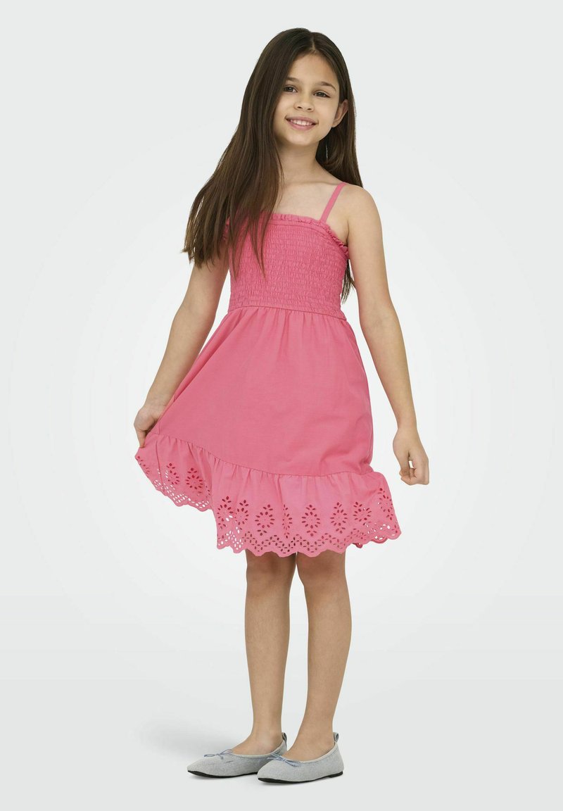 Růžové bavlněné šaty s nařaseným živůtkem a zaobleným lemováním v broderie anglaise. Mají tenké ramínka a volný, áčkový siluetu.