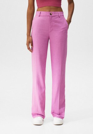 Personne portant un pantalon rose taille haute, jambes droites, avec poches avant, associé à un top court sans manches et des baskets blanches.