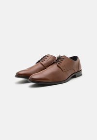 Zapatos de cuero marrón con un acabado suave, punta redonda, tacón bajo y perforaciones decorativas en los laterales. Presentan cierre con cordones.