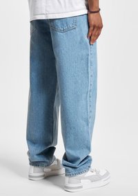 Light blue denim jeans with a loose fit, five-pocket design, and slight fade. Paired with white sneakers featuring gray accents.