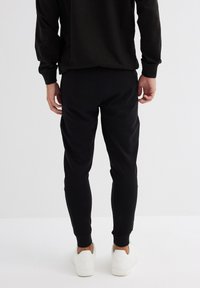 Pantalones de chándal negros con un ajuste slim, banda elástica en la cintura y puños, fabricados en un tejido suave. Combinados con zapatillas blancas.