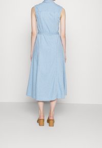 Jasnoniebieska dżinsowa sukienka bez rękawów z paskiem w talii, spódnicą do kolan i kołnierzykiem. Gładka tekstura i prosty design.