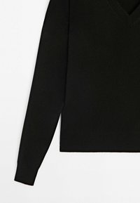 Pull en maille noir avec un col en V, manches longues et ourlet droit. Texture douce, style minimaliste, sans motifs ni embellissements visibles.