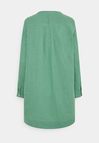 Robe en lin verte à coupe ample, manches longues et détail yoke dans le dos. Elle présente un ourlet arrondi et des poignets boutonnés.