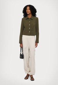 Αχλαδί κάτω σακάκι με ασημένια κουμπιά, σε συνδυασμό με χαλαρές μπεζ παντελόνες και μαύρη τσάντα. Μαύρα σανδάλια με λουριά ολοκληρώνουν την εμφάνιση.