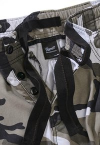 Kaamera lähedalt kaetud printpüksid, millel on elastne vöökoht, must nuppega eesmine sulgur ja must pael, näidates Branditi plaastrit vöökohal.