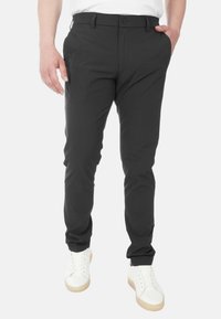Pantaloni neri su misura con una texture liscia, slim fit e chiusura con bottone standard, abbinati a sneaker bianche.