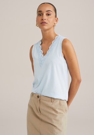 Haut sans manches bleu clair avec un décolleté en V profond et des bordures en dentelle. Tissu doux et lisse. Assorti à une jupe beige avec des poches latérales.