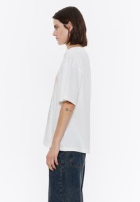 Valge puuvillane oversized t-särk, millel on graafiline trükk. Lühikesed varrukad ja ümar kaelus. Kandmiseks tumedate teksadega.