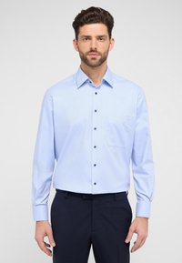 Lichtblauw overhemd met knopen, gemaakt van geweven stof, met een puntkraag, lange mouwen en een borstzak. Donkere knopen contrasteren met de stof.