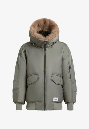 Olívazöld steppelt parkában, műszőrme bélésű kapucnival, cipzáras záródással, két elülső zsebbel és bordázott mandzsettákkal. Az anyag simának és puhának tűnik.