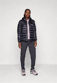 Juodas pūkinis švarkas, turintis prigludusią fasoną, derinamas su šviesiai violetiniu marškinėliu ir tamsiomis krovinių kelnėmis. Avalynė - šviesiai violetiniai žygio batai.