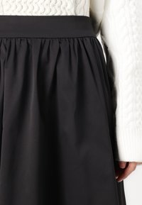 Black, knee-length skirt with a smooth texture and gathered design at the waistband, paired with a white, textured knit sweater.