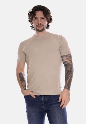 T-shirt in maglia beige a maniche corte con scollatura rotonda, forma aderente e texture a coste. Abbinato a jeans blu.