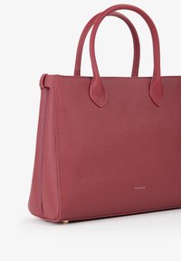 Borsa a tote rossa con texture, manici arrotondati, forma strutturata e un sottile dettaglio del logo metallico nella parte inferiore.
