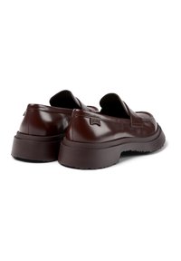 Mocassins en cuir brun foncé avec des semelles en caoutchouc épaisses, des orteils ronds et un petit logo "Camper" sur le côté du talon de chaque chaussure.