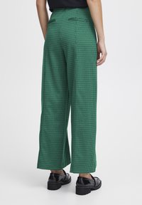 Pantaloni larghi a quadri verdi realizzati in un tessuto morbido, con tasche posteriori e vita alta. Abbinati a scarpe chunky nere.