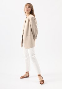 Beige oversize blejzr, bílé úzké kalhoty a hnědé sandály. Měkká látka, přizpůsobený střih a volný fit. Čisté linie s minimem detailů.