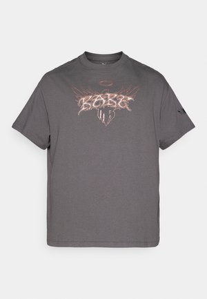 Camiseta de algodón gris con mangas cortas y cuello redondo. Presenta un diseño gráfico con texto y alas en colores contrastantes.