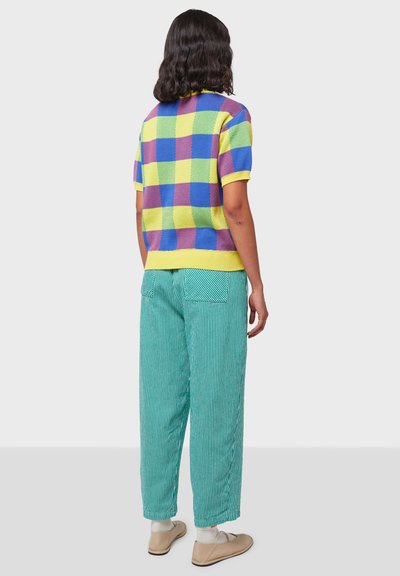 Suéter de punto de manga corta con un patrón de cuadros multicolor en amarillo, azul y púrpura, combinado con pantalones holgados a rayas verdes.