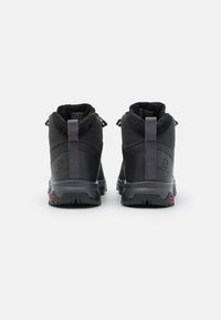 Botas de senderismo negras con un collar acolchado, que cuentan con una suela de goma, parte superior de textil y tirantes en la parte posterior para facilitar su uso.