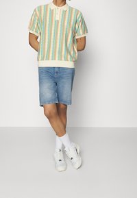 Randig kortärmad polo i flera färger med krämfärgad krage, ihopparad med jeanställning och vita sneakers med grå accenter.