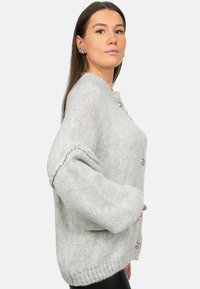 Cardigan a maglia grigia chiara con una trama spessa, maniche lunghe e bottoni arrotondati. Vestibilità comoda e dettagli a coste sull'orlo.