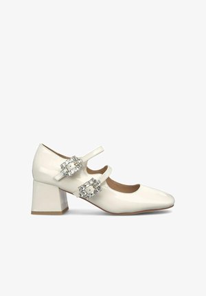 White patent leather Mary Jane shoes with a square toe, low block heel, and two crystal-embellished straps across the instep.