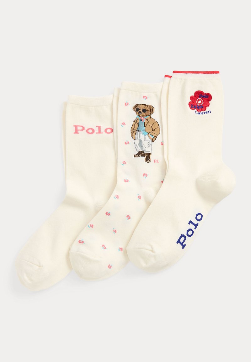 Trois chaussettes couleur crème avec des motifs différents : texte Polo en rose et bleu, un ours portant des lunettes de soleil et des vêtements, et une fleur rouge avec le texte Polo Ralph Lauren.