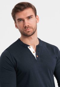 Marinblå långärmad skjorta med vit knappslå; har träknappar, mjukt tyg och en henley-krage design.