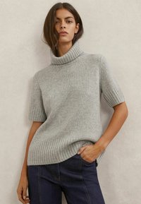 Maglione a maniche corte grigio chiaro con collo alto a costine e orlo a costine, realizzato in tessuto strutturato. Abbinato a jeans in denim blu scuro.