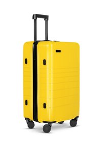 Gelber Hartschalenkoffer mit schlankem Design, schwarzem Reißverschluss und Griff. Verfügt über vier schwarze Räder und Seitengriffe für einfache Mobilität.