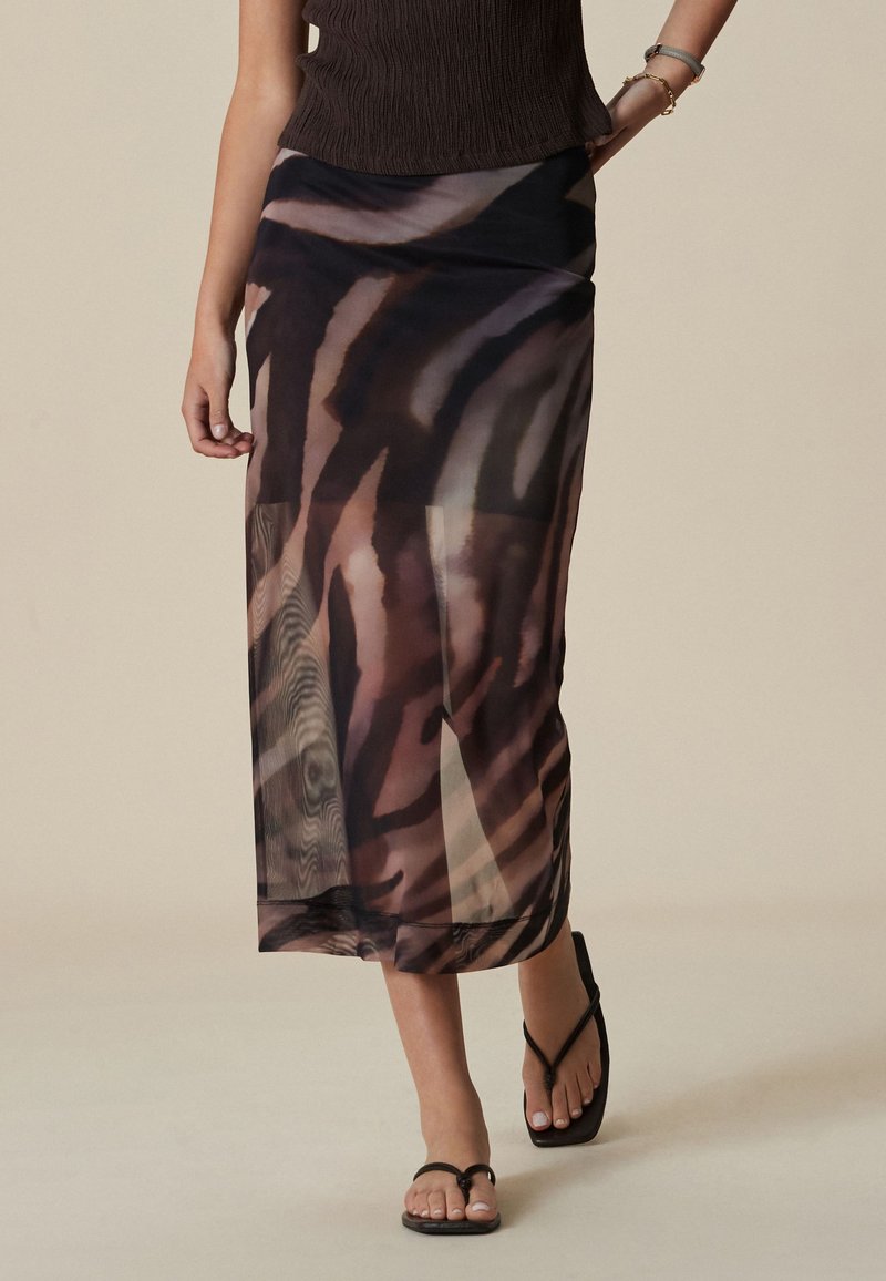 Gonna lunga trasparente multicolore con motivo a strisce di tigre e design fluido. Abbinata a infradito nere e top lavorato.