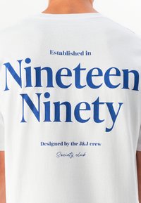 White cotton t-shirt featuring blue text. "Nineteen Ninety" prominently displayed, with smaller text above and below, stating establishment and design info.