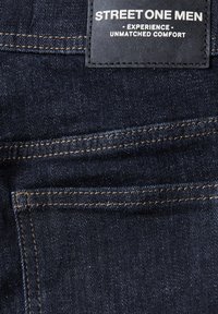 Tmavě modré džínové kalhoty s texturovaným povrchovým zpracováním, s prošívanými švy a koženým štítkem s nápisem "STREET ONE MEN." Čtyři viditelné kapsy.