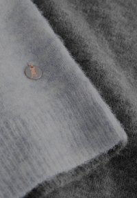 Grijze en lichtblauwe gebreide stofstukken met een zachte textuur, voorzien van een zilveren ronde label met een roze dieren-silhouet en oranje touw.