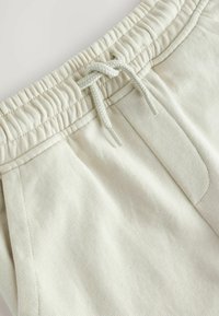 Hellbeige Jogginghosen mit einem elastischen Bund und Kordelzug, flachen Taschen und einer weichen, strukturierten Stoffoberfläche.